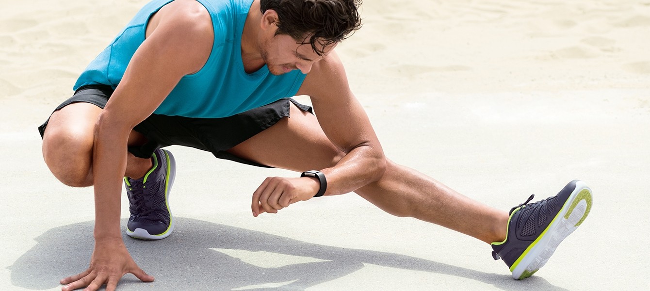 Sportler beim Dehnen mit Blick auf Fitnesstracker