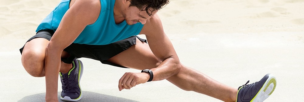 Sportler beim Dehnen mit Blick auf Fitnesstracker